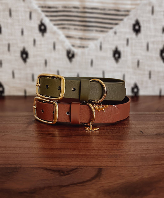 Two biothane dog collars, one green and one brown, on a wooden surface with a patterned rug in the background.
